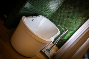 A modern bathroom with a white bathtub, a green tiled wall, and a wooden floor.