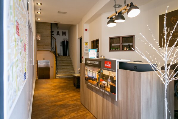 Zona de recepción de un hotel con un mostrador de madera, una escalera al fondo y un cartel que indica que el hotel pertenece a la cadena 'Top Hotels'.