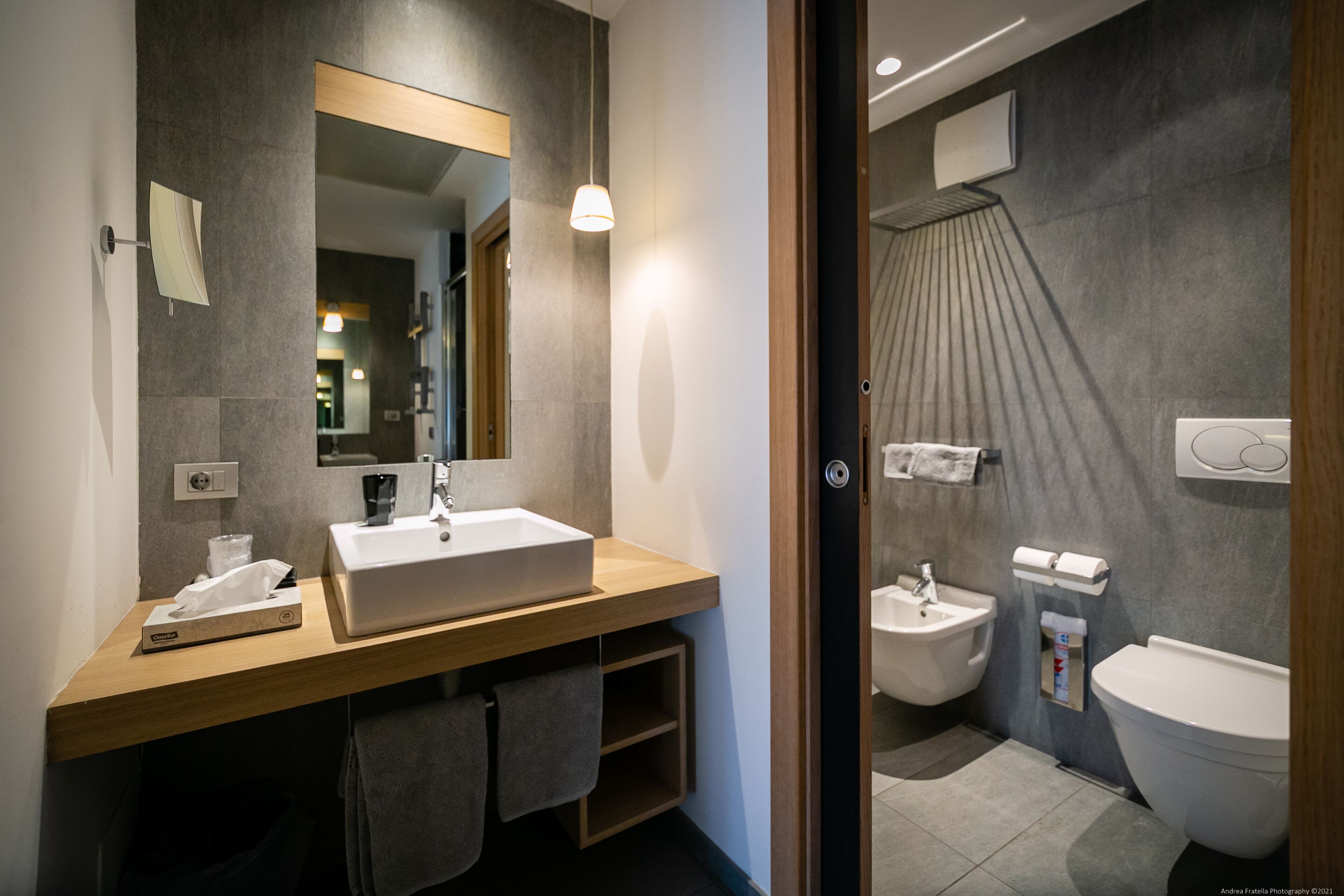 Un baño moderno con tocador de madera, un espejo grande, un lavamanos, un bidé y un inodoro.