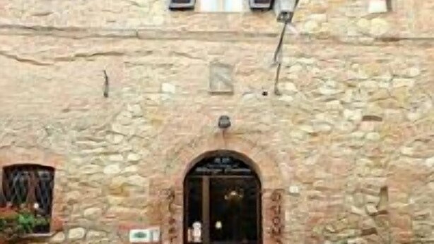 A stone building with a central arched entrance, multiple windows, and potted plants at the entrance. - Albergo Duomo (Montepulciano)