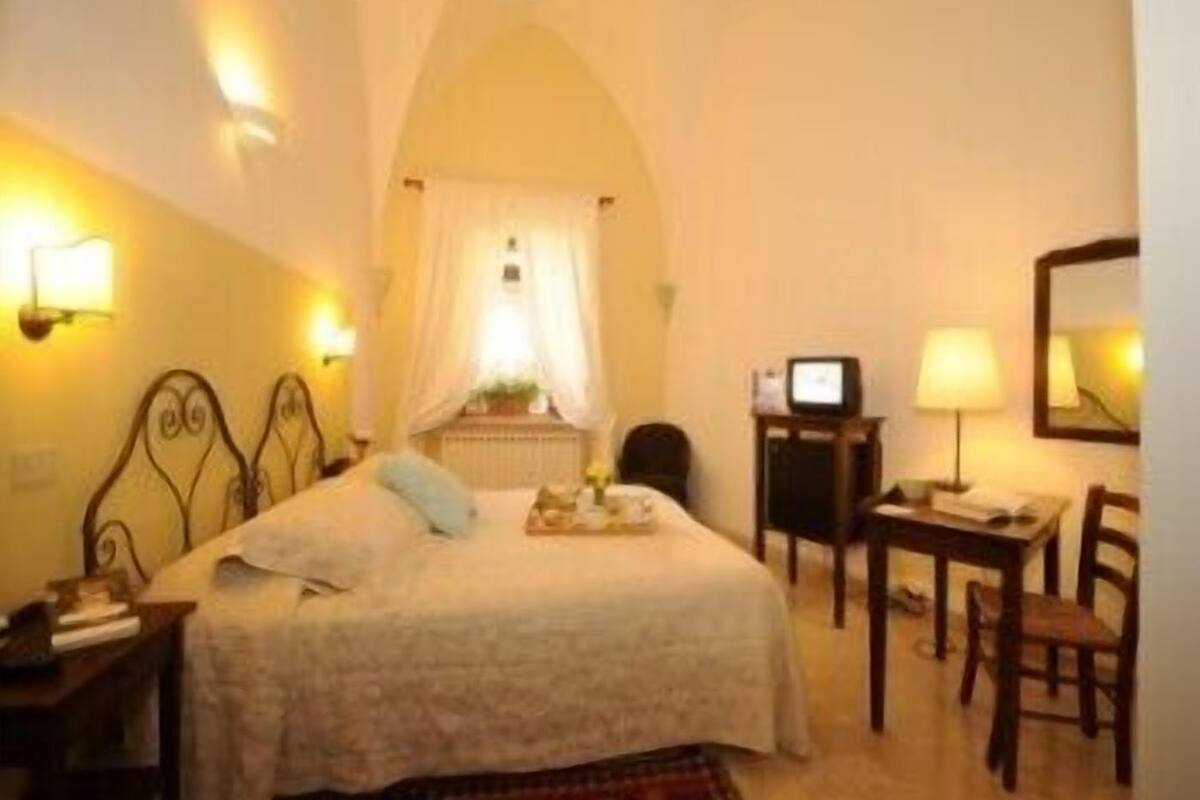 A hotel room with a bed, a desk with a computer, a chair, and a lamp.