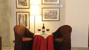 A room with two leather chairs, a small table with a red tablecloth, and a wine bottle and glass on the table. - Albergo Duomo (Montepulciano)