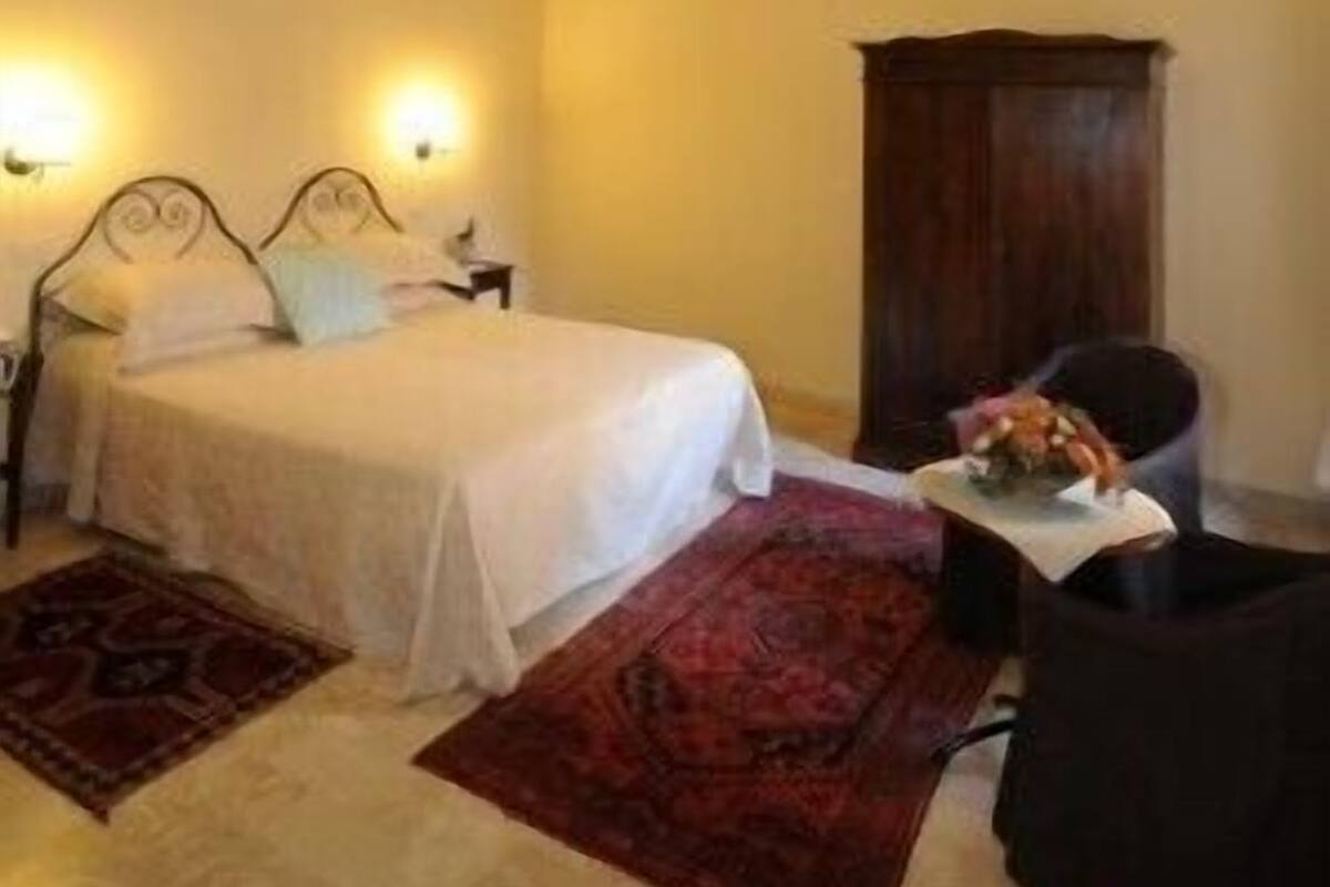A bedroom with a bed, bedside lamps, a nightstand, a red rug, and a wooden cabinet.