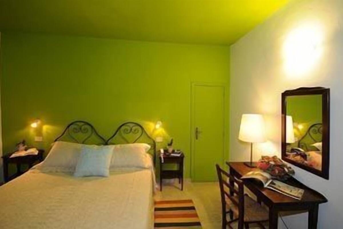 A room with a bed, bedside tables, a desk, a chair, a lamp, and a mirror.