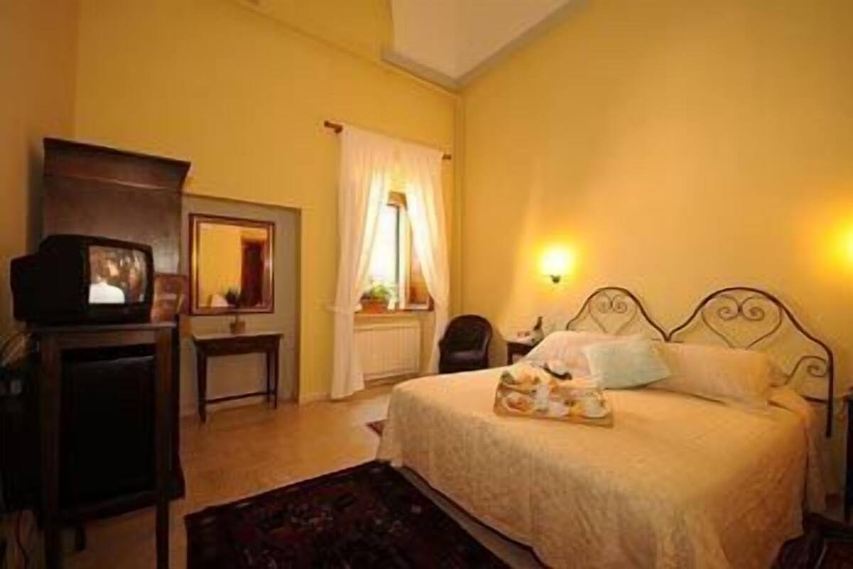 A bedroom with a bed, a television, a desk, and a window with curtains.