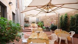 An outdoor patio area with tables and chairs, surrounded by plants and a stone wall. - Albergo Duomo (Montepulciano)