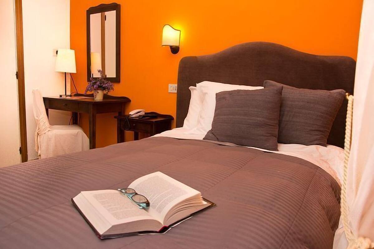 A hotel room with a large bed, a bedside table with a lamp, a mirror, and a nightstand with a phone.
