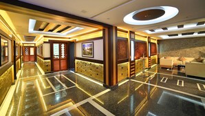 A hotel lobby with a polished marble floor, a reception desk, and a seating area with sofas. - Elysium Gardens Hill Resorts (Devikolam)