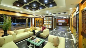 A hotel lobby with a reception desk, seating area, and a view of parked cars outside. - Elysium Gardens Hill Resorts (Devikolam)