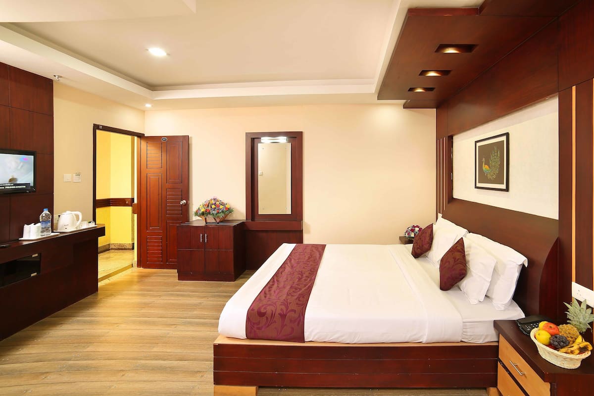 A hotel room with a wooden bed, a desk with a computer, a mirror, and a wall-mounted TV.
