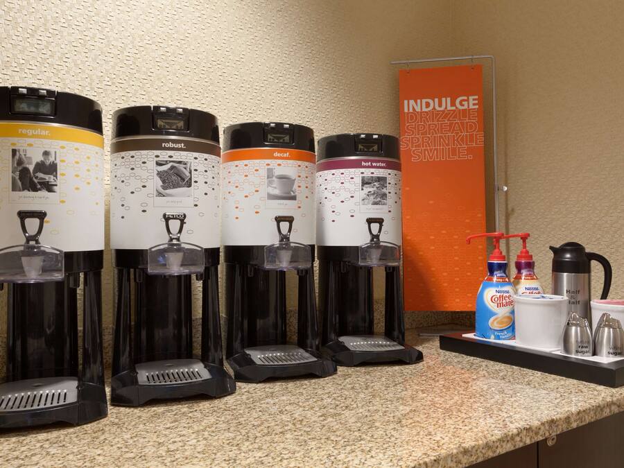 Four coffee dispensers labeled regular, robust, decaf, and hot water, along with a coffee maker, sugar, and creamer on a countertop.