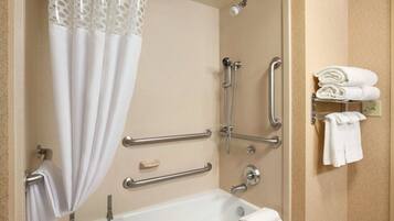 A bathroom with a bathtub, grab bars, a showerhead, and a towel rack.