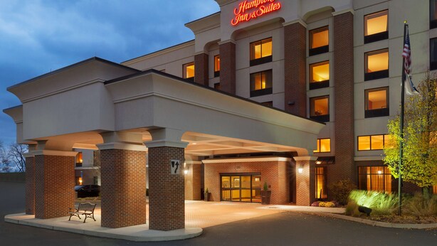 Un Hampton Inn & Suites con fachada de ladrillo, ventanas grandes y una entrada bien iluminada.