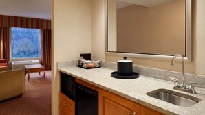 Habitación de hotel con cocina, mesa de comedor, sofá y un amplio ventanal con cortinas.