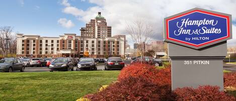 A Hampton Inn & Suites sign with a parking lot and a building in the background.