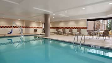 Una piscina interior con borde de baldosas a cuadros, sillas de descanso y una mesa con sillas.