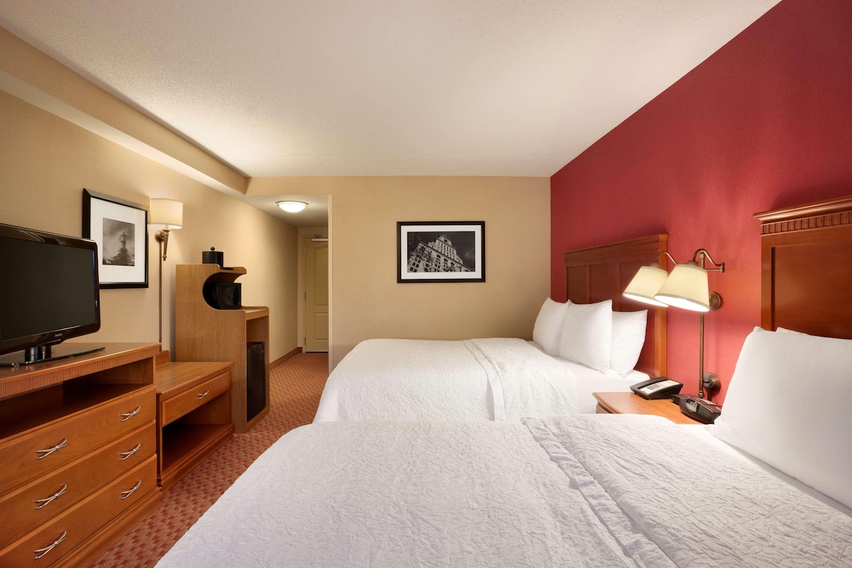 A hotel room with two beds, a television, a desk, and a lamp.