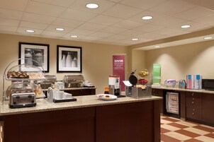 Zona de buffet con diferentes estaciones de comida, que incluyen un tostador, una máquina de café y un mostrador refrigerado.