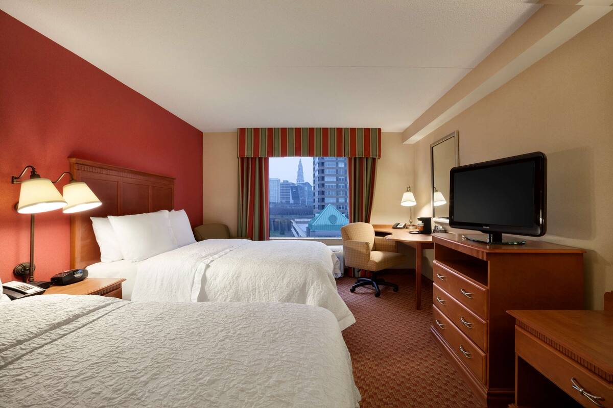 Une chambre d’hôtel avec deux lits, un bureau, une chaise, une télévision et une fenêtre donnant sur la ville.