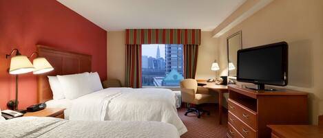 A hotel room with two beds, a desk, a chair, a television, and a window with a city view.