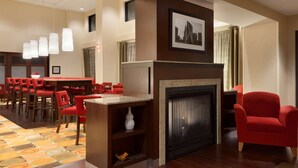 Vestíbulo de hotel con chimenea, sillas rojas, zona de comedor y alfombra estampada.