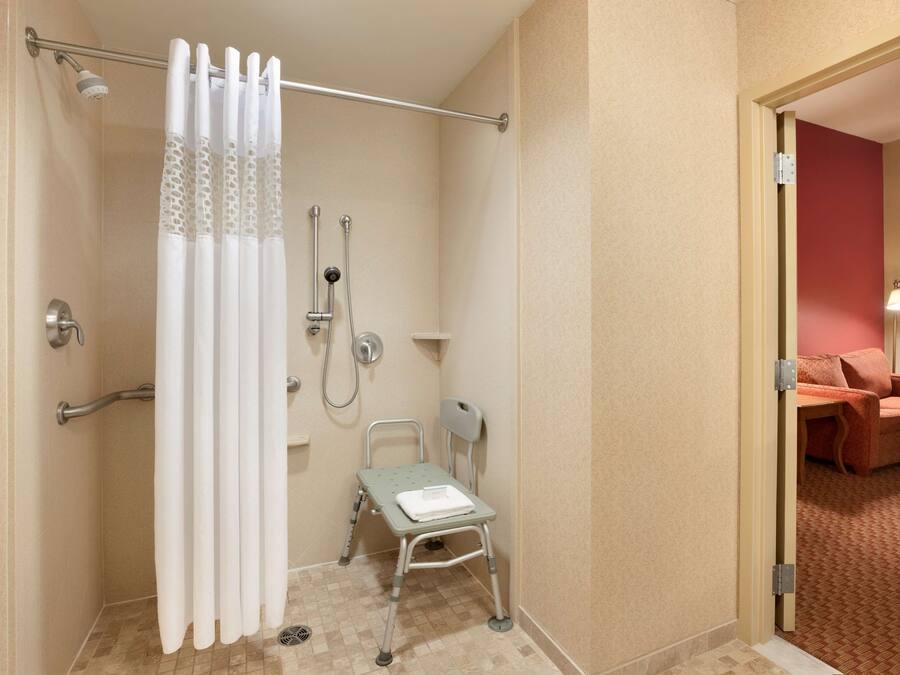 A shower area with a wheelchair, a showerhead, and a towel rack.
