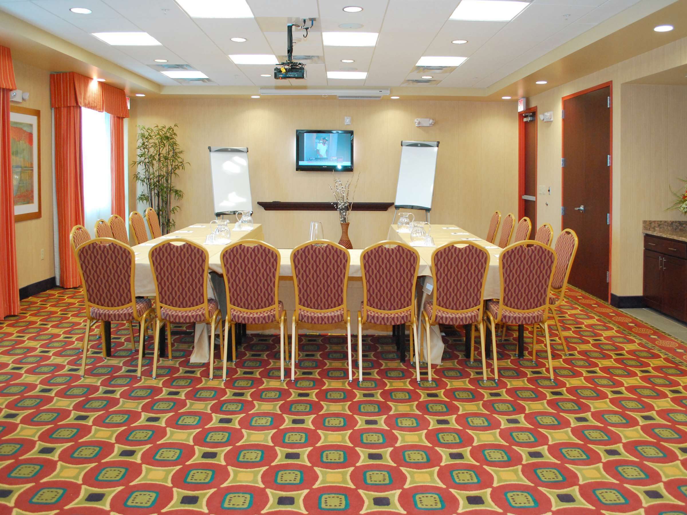 Una sala de conferencias con una amplia mesa, sillas, una pantalla de televisión y un proyector.