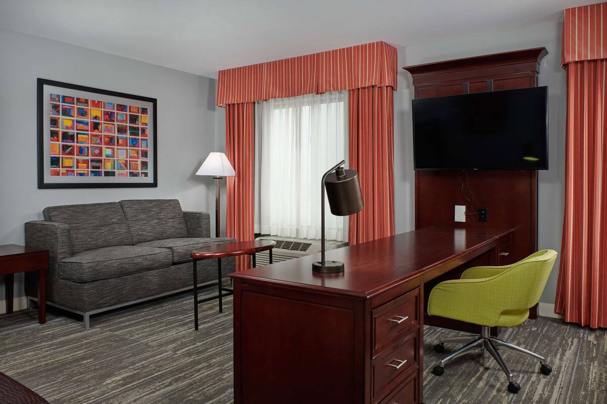 A hotel room with a sofa, a desk with a chair, a TV, and a framed picture on the wall.