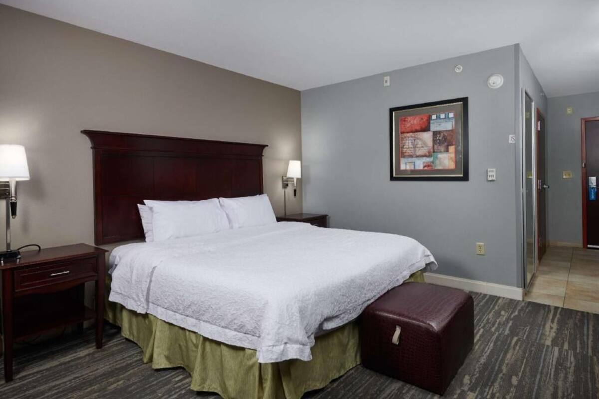 A hotel room with a large bed, two bedside tables, a nightstand, a framed picture on the wall, and a door leading to another room.