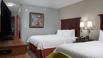 A hotel room with two beds, a TV, a painting on the wall, and a desk with a lamp.