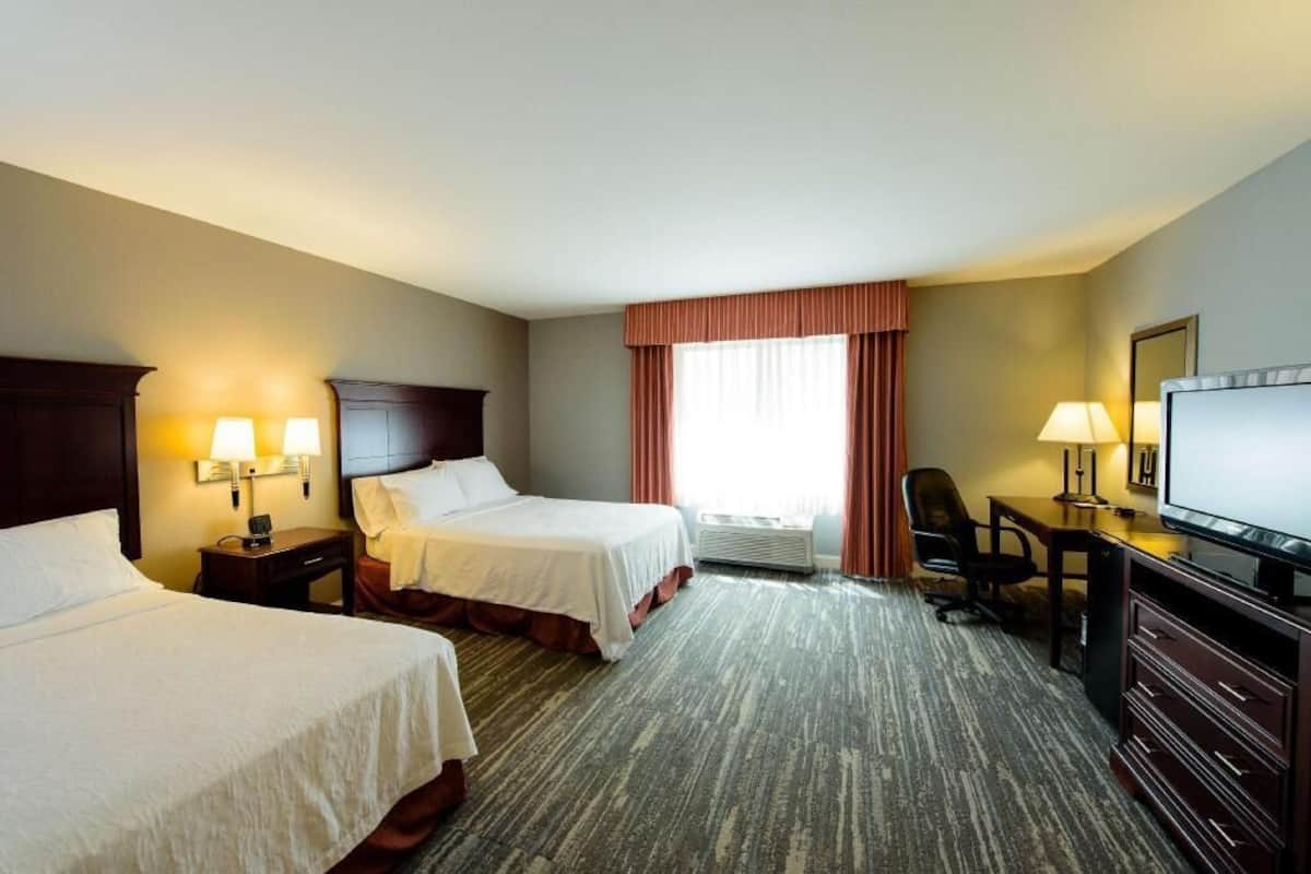 A hotel room with two beds, a desk, a television, and a window with curtains.