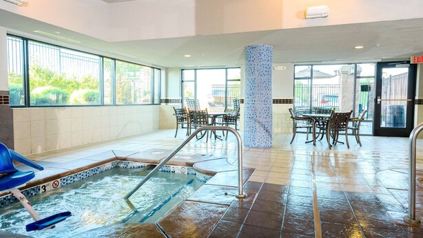 A pool area with a hot tub, seating, and a view of the outdoors.