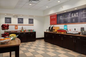 A clean, well-lit kitchen area with a checkered floor, dark wooden cabinets, and various food items displayed on the counter. - Hampton Inn & Suites Denver/Highlands Ranch (Littleton)