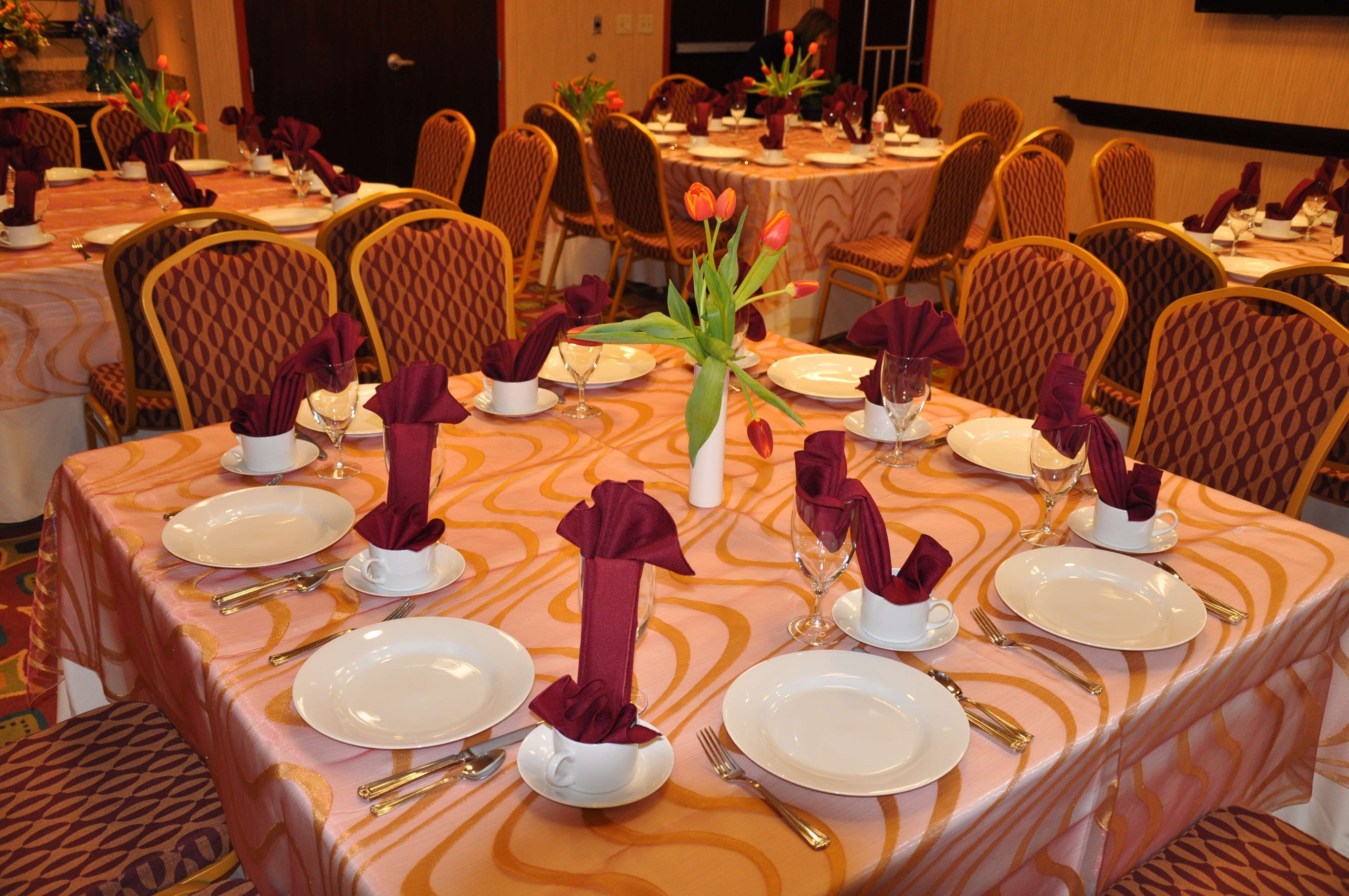 A banquet hall with round tables set for dining, each with white plates, gold cutlery, and red napkins.