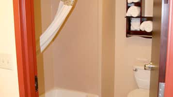A bathroom with a bathtub, toilet, and a shelf with towels.
