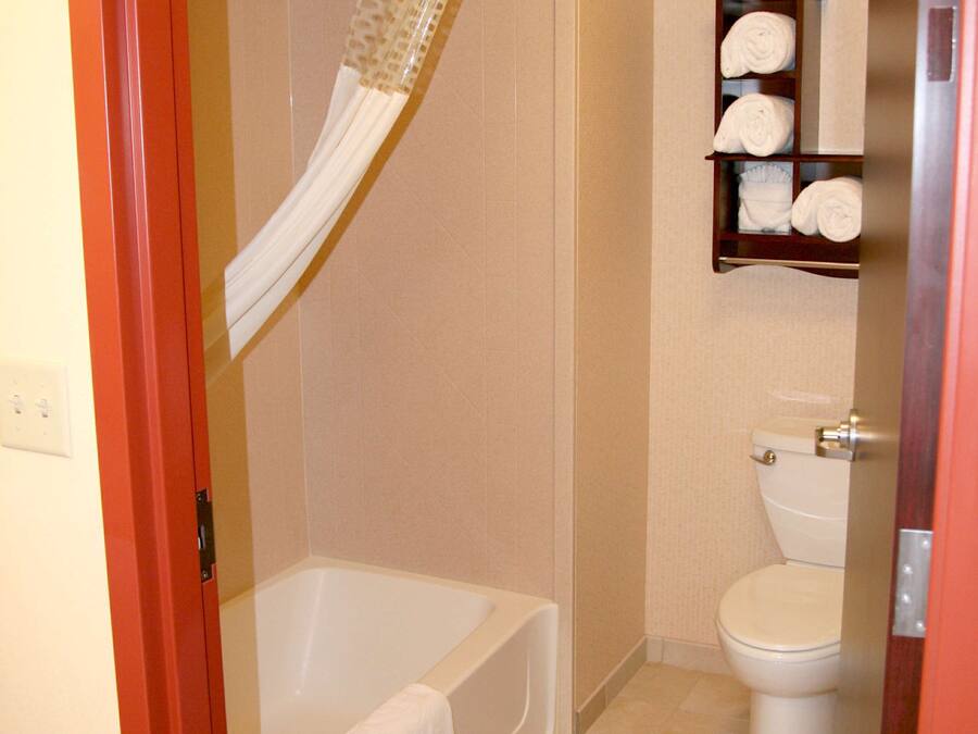 A bathroom with a bathtub, toilet, and a shelf with towels.