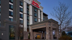 A Hampton Inn & Suites building with a clear entrance, a sign indicating a 14-foot clearance, and a parking area with a blue shuttle visible.