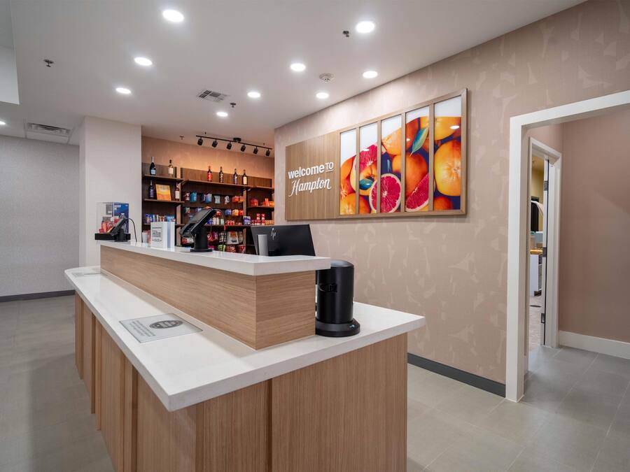 Mostrador de recepción de hotel con mostrador de madera, una máquina de café y un cartel en la pared dando la bienvenida a los huéspedes a Hampton.