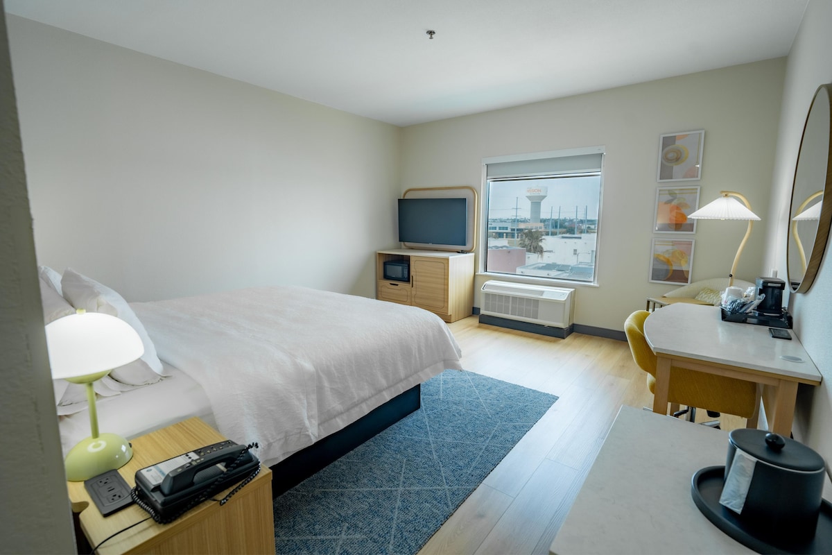 A hotel room with a bed, desk, chair, desk lamp, telephone, and a television.