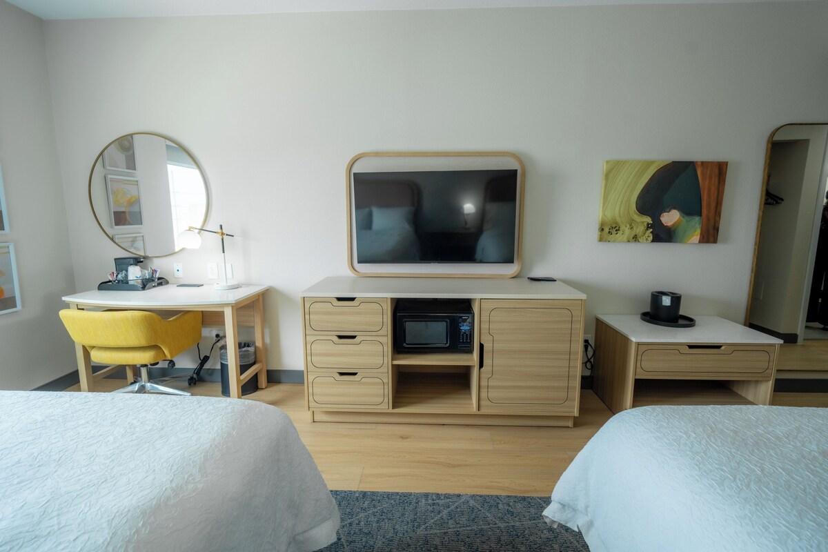 Habitación de hotel con dos camas, un escritorio con silla, microondas y televisión.