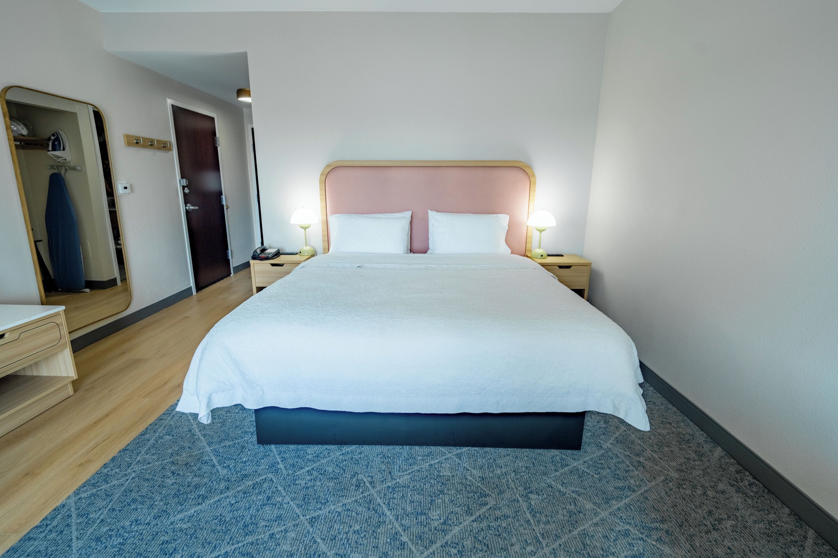A hotel room with a large bed, bedside tables with lamps, a wardrobe, and a mirror.