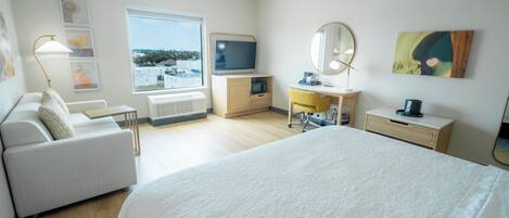 Une chambre d’hôtel moderne dotée d’un grand lit, d’un canapé, d’un bureau, d’une télévision et offrant une vue sur la ville.
