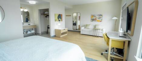 Quarto de hotel com cama, escrivaninha, cadeira e televisão.