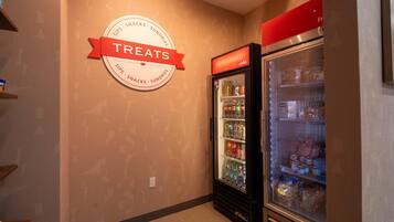 A wall with a circular sign indicating a treats section, a refrigerator stocked with beverages and snacks, and a shelf with packaged items.