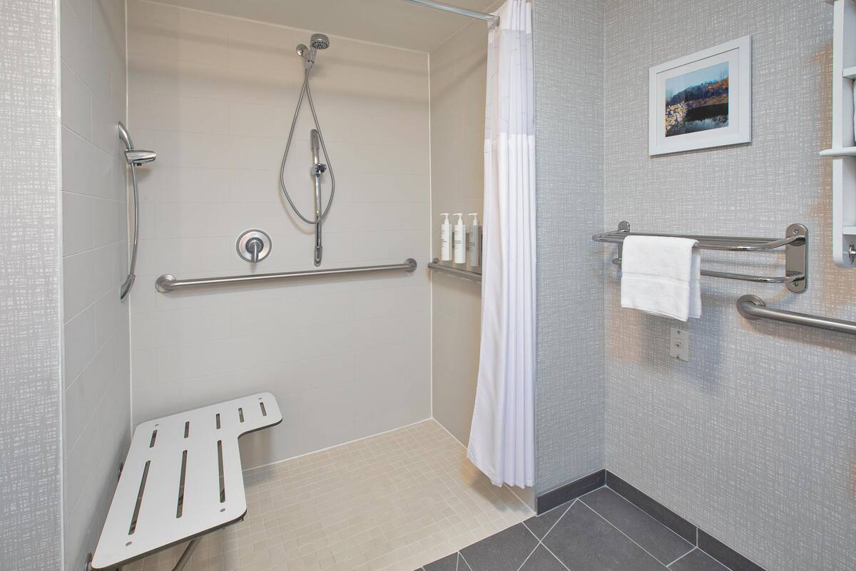 A bathroom with a shower, grab bars, a white towel rack, and a picture on the wall.