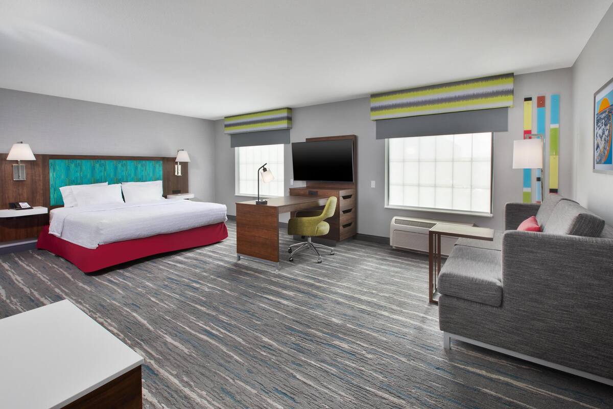 A hotel room with a bed, desk, chair, TV, and a sofa.