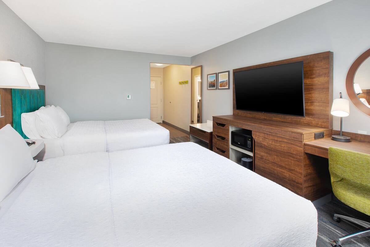 A hotel room with two beds, a TV, a desk, and a mirror.