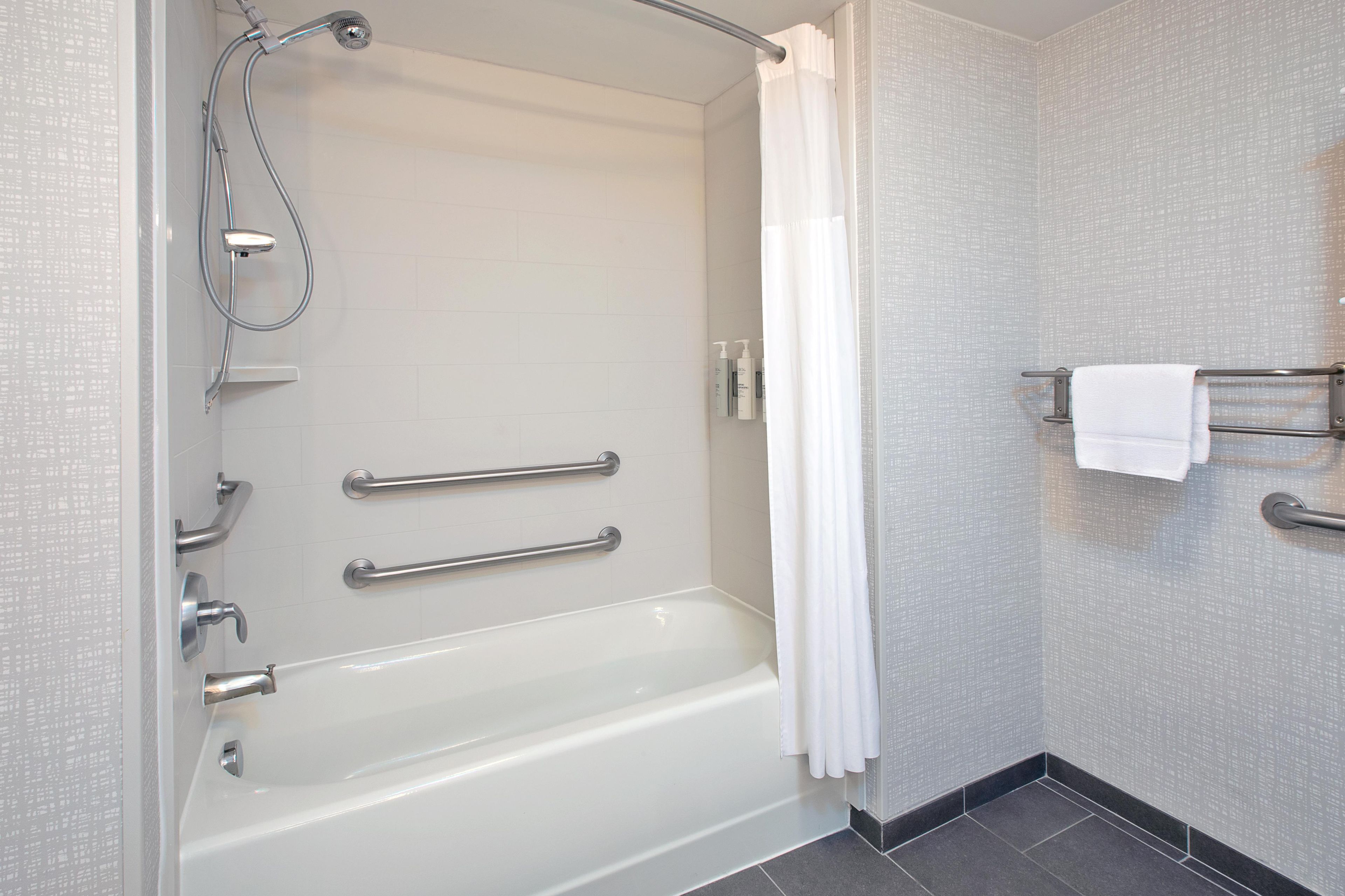 Ein modernes Badezimmer mit einer Badewanne, Haltegriffen, einer Duschbrause und einem Handtuchhalter.