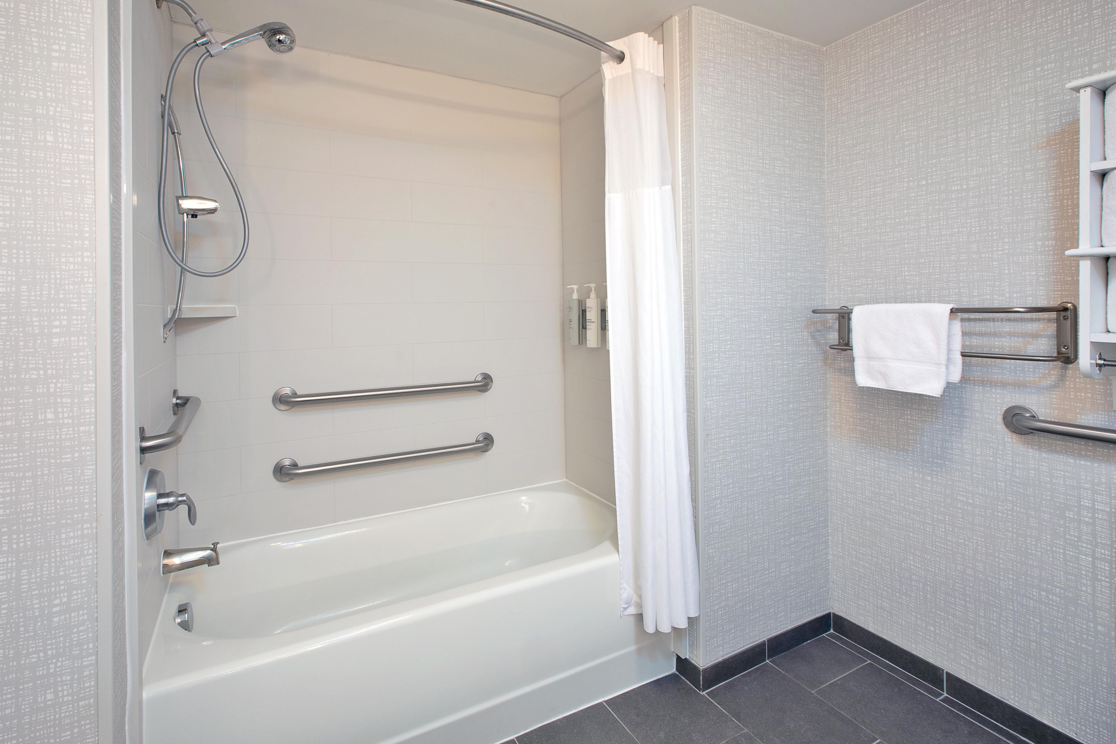 A modern bathroom with a bathtub, grab bars, a shower head, and a towel rack.