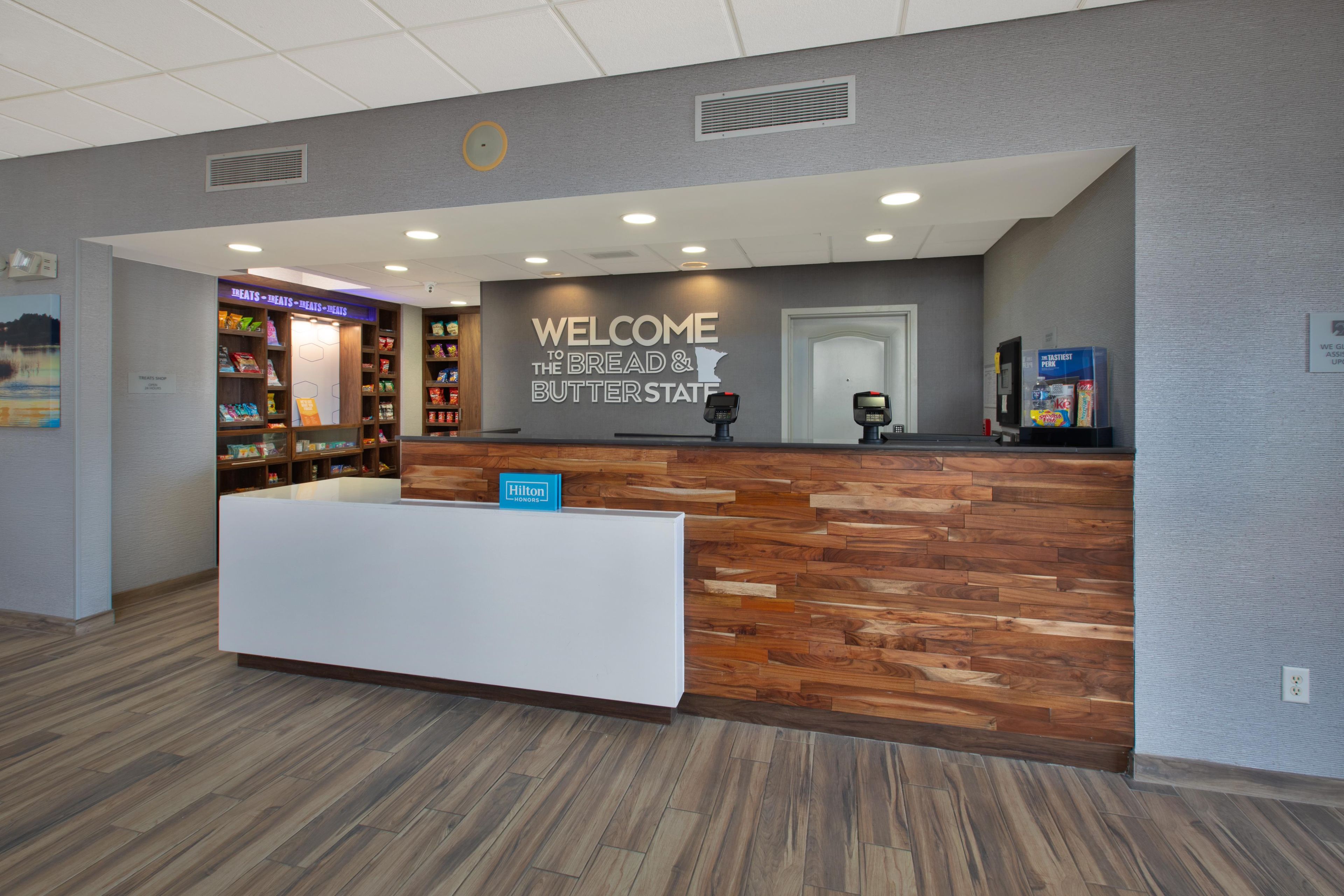 Una mesa de recepción con un cartel que dice 'Welcome to the Bread & Butter State', un cartel de 'Hilton Honors' y un cartel de 'Treats Shop'.